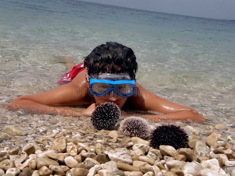 Portrait of a boy lying in the shallow waters in the crystal clear blue Adriatic sea (Croatia - Dalmatia) with a diving mask and watching their catch - sea urchins. - spending summer holidays. Horizontal color photo. Portrait of a boy lying in the shallow waters in the crystal clear blue Adriatic sea (Croatia - Dalmatia) with a diving mask and watching their catch - sea urchins. - spending summer holidays. Horizontal color photo.