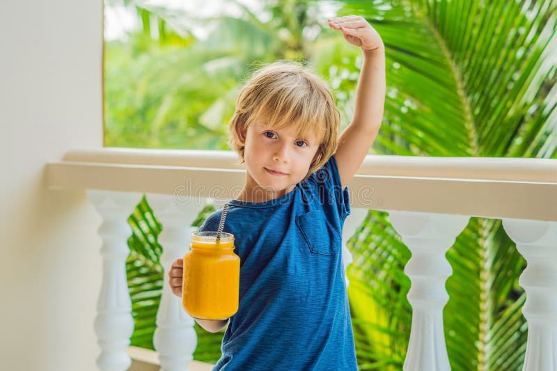 Chłopiec trzyma kamieniarza słój mangowi smoothies w jego ręce i pokazuje obraz stock Chłopiec trzyma kamieniarza słój mangowi smoothies w jego ręce i pokazuje obraz stock