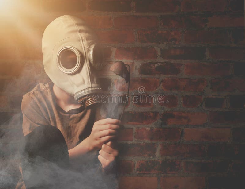 A young boy is holding a dead flower against a brick wall with a gas mask and dangerous gas in the air for a global warming or destruction concept. A young boy is holding a dead flower against a brick wall with a gas mask and dangerous gas in the air for a global warming or destruction concept.