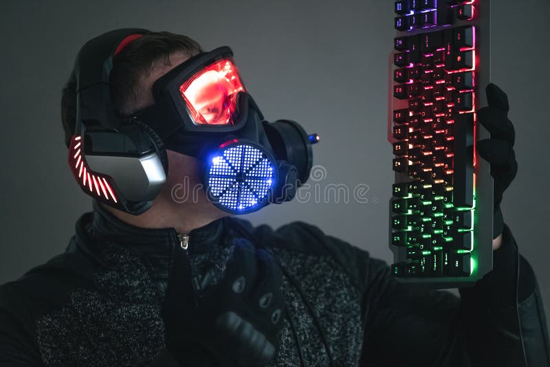 Futuristic man in led light helmet with a computer keyboard in hands over dark background. Cyberpunk concept. Futuristic man in led light helmet with a computer keyboard in hands over dark background. Cyberpunk concept