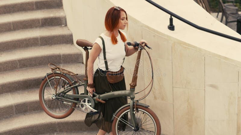 Ciclista de la mujer que camina abajo de las escaleras y que sostiene la bicicleta en brazos Ciudad de la bici de la mujer imagen de archivo libre de regalías Ciclista de la mujer que camina abajo de las escaleras y que sostiene la bicicleta en brazos Ciudad de la bici de la mujer imagen de archivo libre de regalías