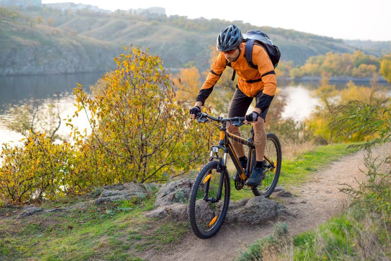 Ciclista na laranja que monta o Mountain bike em Autumn Rocky Trail Esporte extremo e conceito Biking de Enduro fotografia de stock Ciclista na laranja que monta o Mountain bike em Autumn Rocky Trail Esporte extremo e conceito Biking de Enduro fotografia de stock