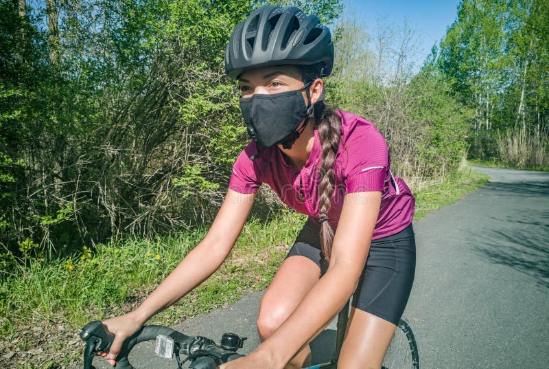 Sport cyclist woman biking on road bike wearing face mask for Covid-19 prevention during summer outdoor recreational activity. Fitness outside. Sport cyclist woman biking on road bike wearing face mask for Covid-19 prevention during summer outdoor recreational activity. Fitness outside.