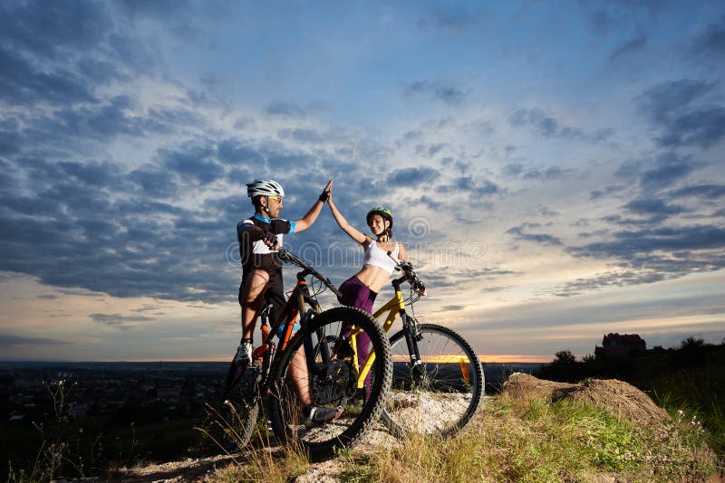 Ciclistas positivos que sorriem e que highing cinco em bicicletas imagem de stock royalty free Ciclistas positivos que sorriem e que highing cinco em bicicletas imagem de stock royalty free