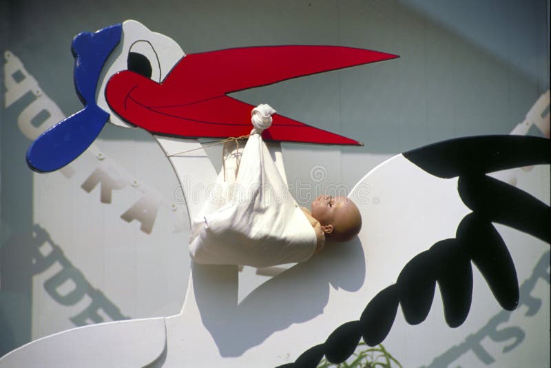 LEERDAM,HOLLAND-SEPTEMBER 14, 2021:Classic depiction in wood of a stork in flight delivering a newborn baby. In Holland new parents put this wooden stork in their front yard. LEERDAM,HOLLAND-SEPTEMBER 14, 2021:Classic depiction in wood of a stork in flight delivering a newborn baby. In Holland new parents put this wooden stork in their front yard