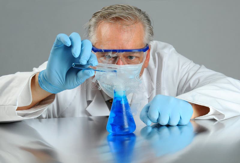 Closeup of a mad scientist pouring a liquid from a test tube into a beaker that is emitting smoke. Horizontal format. Closeup of a mad scientist pouring a liquid from a test tube into a beaker that is emitting smoke. Horizontal format.