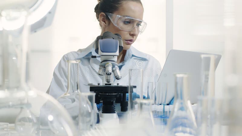 Científica utilizando microscopio y portátil en el laboratorio fotos de archivo libres de regalías