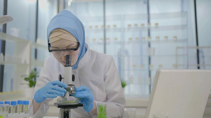 Científico musulmán en un laboratorio moderno trabaja en una laptop y un microscopio