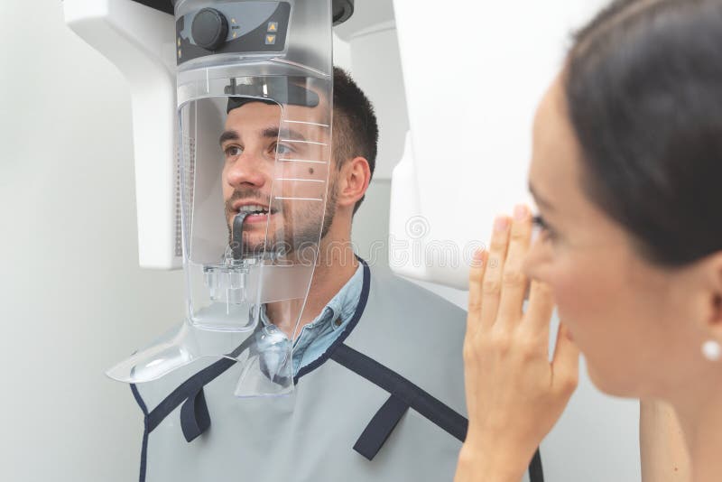 Cierpliwa pozycja w promieniowanie rentgenowskie maszynie przy stomatologiczną kliniką fotografia stock Cierpliwa pozycja w promieniowanie rentgenowskie maszynie przy stomatologiczną kliniką fotografia stock