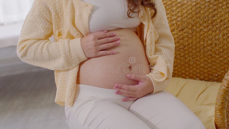 Cierra a una mujer embarazada feliz sentada en la cama sosteniendo y acariciando su gran vientre en casa embarazo de una mujer jov metrajes