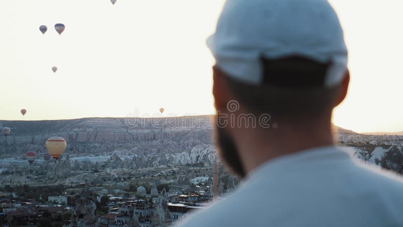 Cierre atmosférico de un joven turista mirando un globo de aire caliente flotando a la temprana luz del amanecer en cappadocia