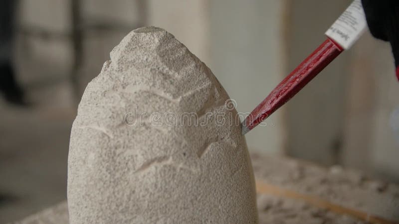 Cierre de las manos de los hombres haciendo una escultura de piedra usando un cincel en un taller.