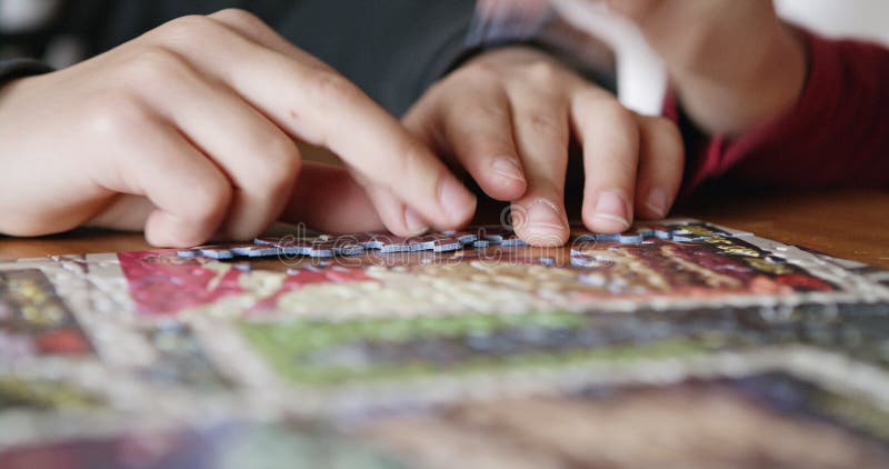 Cierre de las manos de los niños trabajando juntos en un rompecabezas en una mesa interior