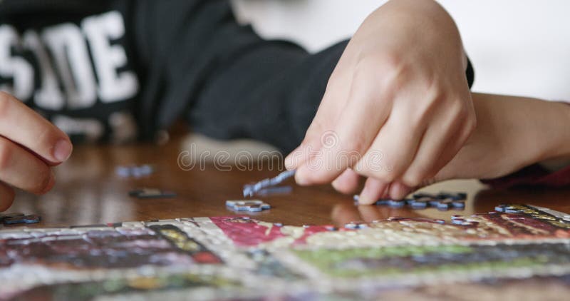 Cierre de las manos de los niños trabajando juntos en un rompecabezas en una mesa interior