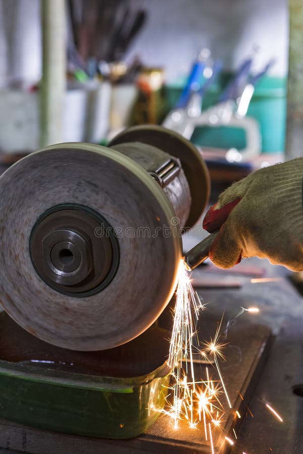 Cierre de las manos de un técnico profesional utilizando una máquina de pulir metálico para barras metálicas afiladas con chispas imagenes de archivo