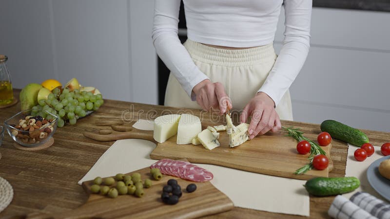 Cierre de manos femeninas en el marco. un ama de casa en la cocina corta trozos de queso y prepara aperitivos para una fiesta