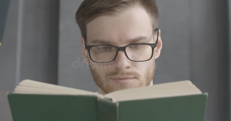Cierre de un hombre caucásico con anteojos leyendo libro y sonriendo. rostro lento de lector joven inteligente disfrutando