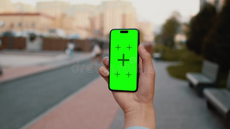 Cierre de una mano sosteniendo un smartphone con una pantalla verde de burla con una acera de una calle de la ciudad en un día sol metrajes