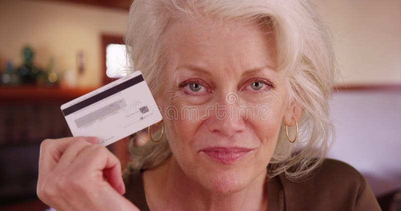 Cierre de una mujer madura sosteniendo una tarjeta de crédito sonriendo a cámara en el salón almacen de video