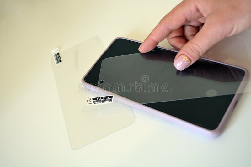 Close-up of a woman's hand gluing a protective glass on a cell phone with a pink case. Close-up of a woman's hand gluing a protective glass on a cell phone with a pink case