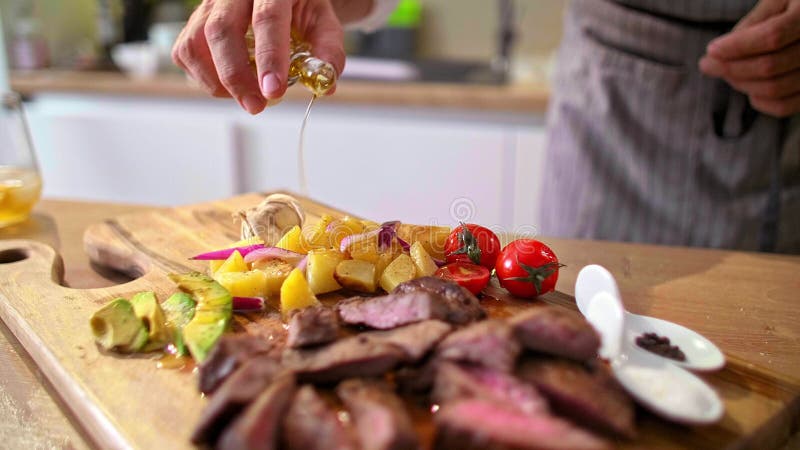 Cierre del chef añadiendo aceite de oliva a la carne asada en una tabla de madera almacen de video
