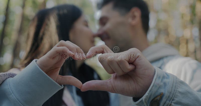 Cierre del símbolo del corazón hecho con manos y pareja borrosa hombre y mujer besándose al aire libre