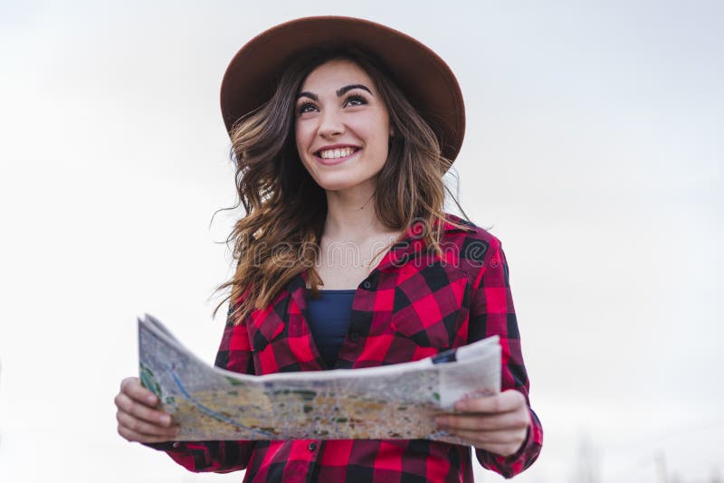 Cierre el retrato de una joven hermosa mujer vestida de forma casual, mirando un mapa, usando un moderno sombrero hipster. Diversi foto de archivo libre de regalías