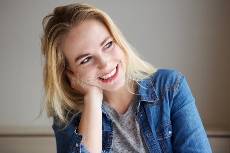 Cierre encima de la mujer rubia joven sonriente que se inclina a mano y que mira lejos imágenes de archivo libres de regalías Cierre encima de la mujer rubia joven sonriente que se inclina a mano y que mira lejos imágenes de archivo libres de regalías