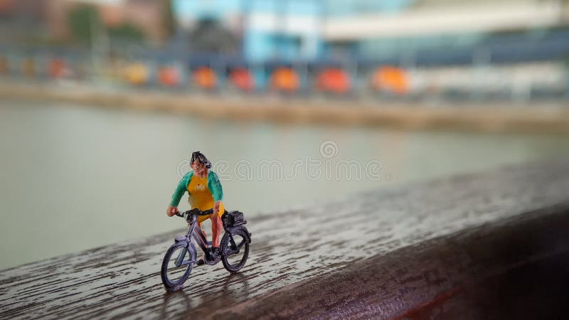 Cierre encima de los juguetes de Mini Figure Woman que montan en bicicleta en la manera de la trayectoria del lado del río con el fotografía de archivo Cierre encima de los juguetes de Mini Figure Woman que montan en bicicleta en la manera de la trayectoria del lado del río con el fotografía de archivo