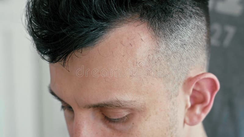 Cierre extremo encima de la cara del hombre en salón de la peluquería El peluquero corta el pelo por las podadoras