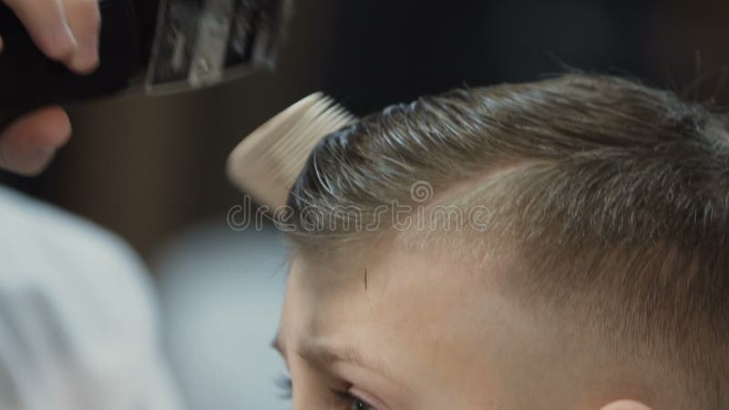 Cierre para arriba El peluquero peina el pelo del cliente en la barbería con el peine Perfil del niño pequeño que hace su peinado