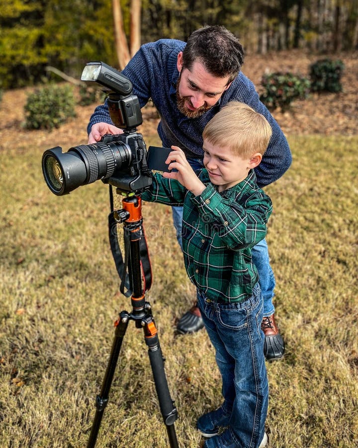 Cierre vertical de un padre enseñando a su hijo con una cámara de trípode profesional al aire libre fotografía de archivo