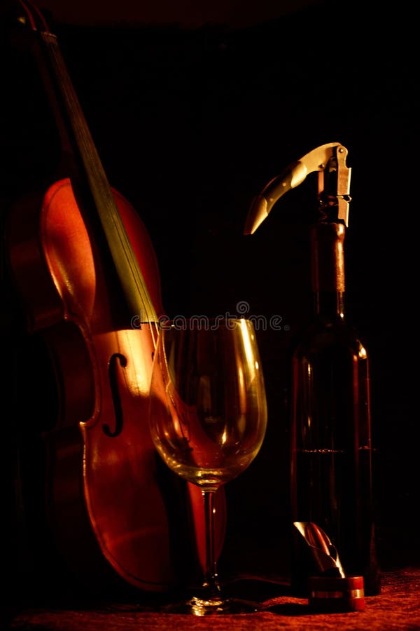 Cierre vertical de un violín una botella de vino y un vaso con fondo negro imagen de archivo