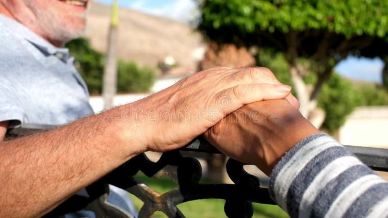 Cierre y retrato de dos manos temblando juntas y personas mayores y maduras hablando en un banco y divirtiéndose - tomando c almacen de metraje de vídeo