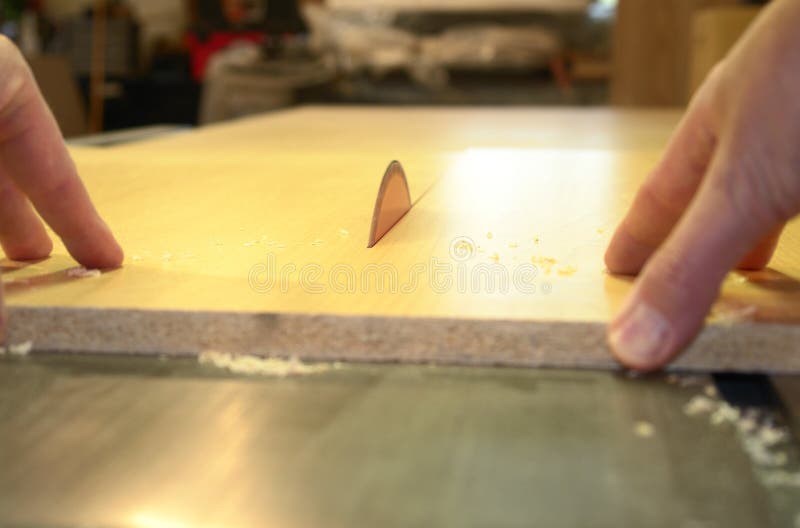 Hands pushing a sheet of maple melamine through a table saw. Hands pushing a sheet of maple melamine through a table saw