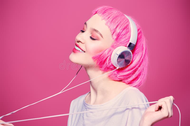 Trendy girl with pink hair enjoys the music on headphones. Pink background. Youth style, leisure. Trendy girl with pink hair enjoys the music on headphones. Pink background. Youth style, leisure.