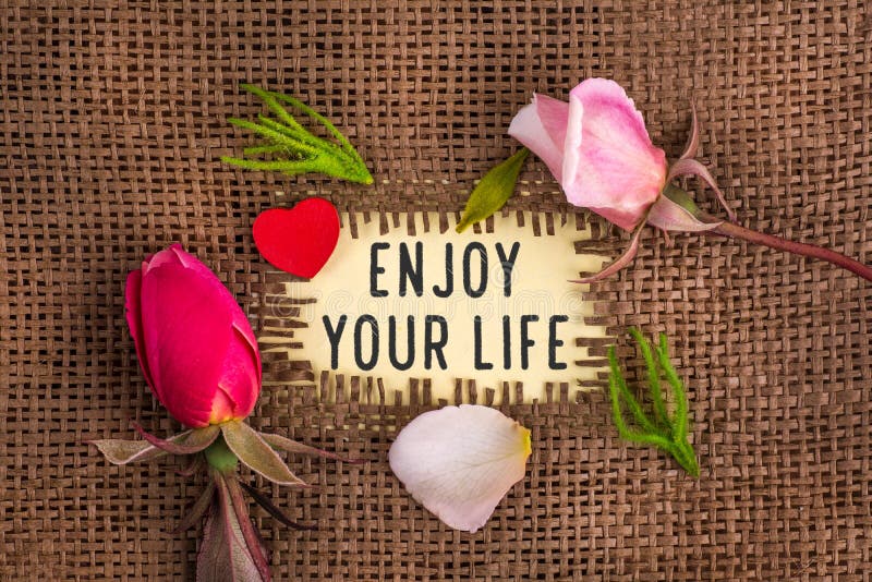 Enjoy your life written in hole on the burlap with rose flowers and wooden red heart. Enjoy your life written in hole on the burlap with rose flowers and wooden red heart