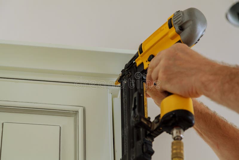Carpenter brad using nail gun to Crown Moulding on kitchen cabinets framing trim, with the warning label that all power tools have on them shown illustrating safety concept. Carpenter brad using nail gun to Crown Moulding on kitchen cabinets framing trim, with the warning label that all power tools have on them shown illustrating safety concept