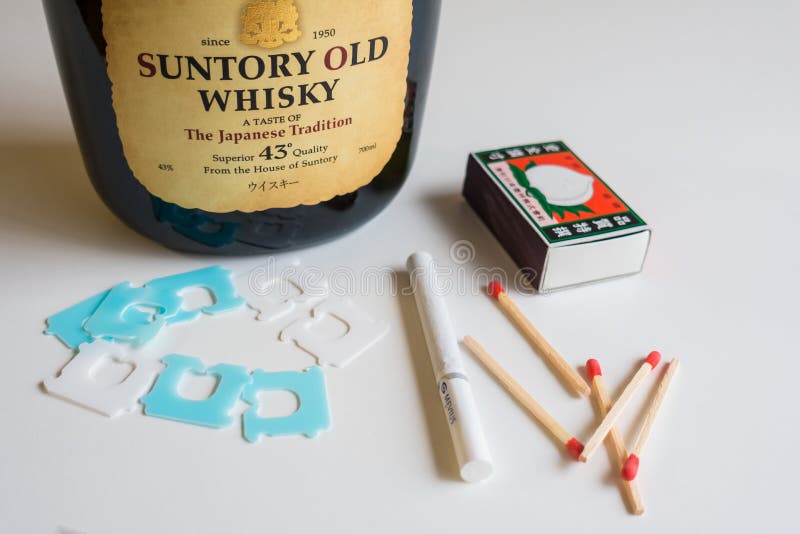 Beppu, Japan, November 11,2017: Composition with objects of cigarettes, matches and Japanese whiskey on a white table. Beppu, Japan, November 11,2017: Composition with objects of cigarettes, matches and Japanese whiskey on a white table