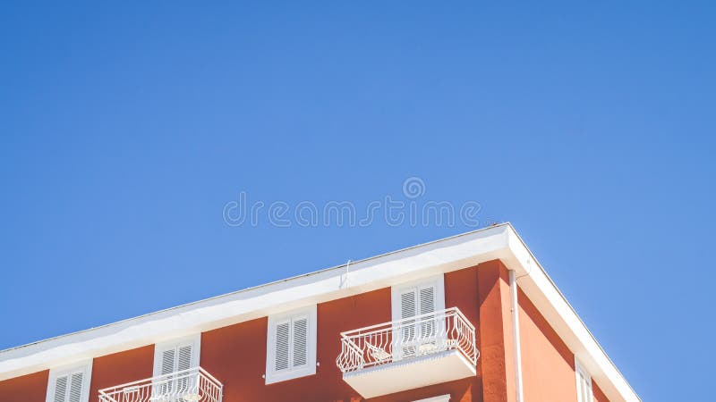 Cima di una costruzione arancio con un balcone bianco e della finestra con chiaro cielo blu nei precedenti fotografia stock libera da diritti Cima di una costruzione arancio con un balcone bianco e della finestra con chiaro cielo blu nei precedenti fotografia stock libera da diritti
