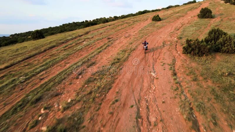 Cinematic flight behind a cross bike going off-road. Summer sunset. Climb to the top of the mountain.