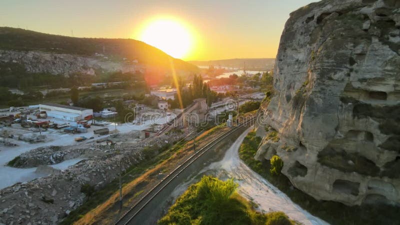 Cinematic flight at sunset near a white cliff and an empty railway. Lovely sun glare. Monastery in the rock. The departing train.