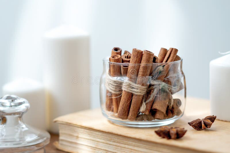 Cinnamon sticks in glass jar, anise star, candles, vintage book on old rustic rustic wooden background.