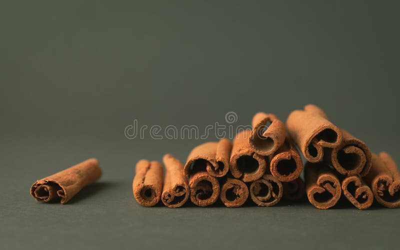 Cinnamon sticks stacked in a pile on the dark green background