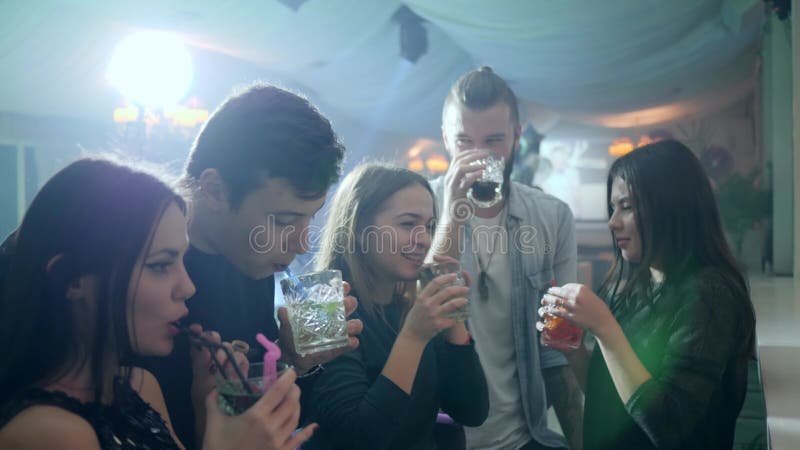 Cinq amis gais font un pain grillé avec les cocktails alcooliques et ont l'amusement dans un club près au compteur de barre