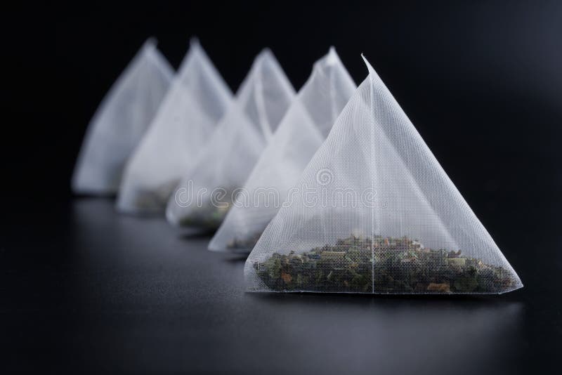 Cinque sacchetti da tè piramidali con tè verde su fondo di cucina scuro. macro. stile scuro. una bevanda per palangari. chiusura