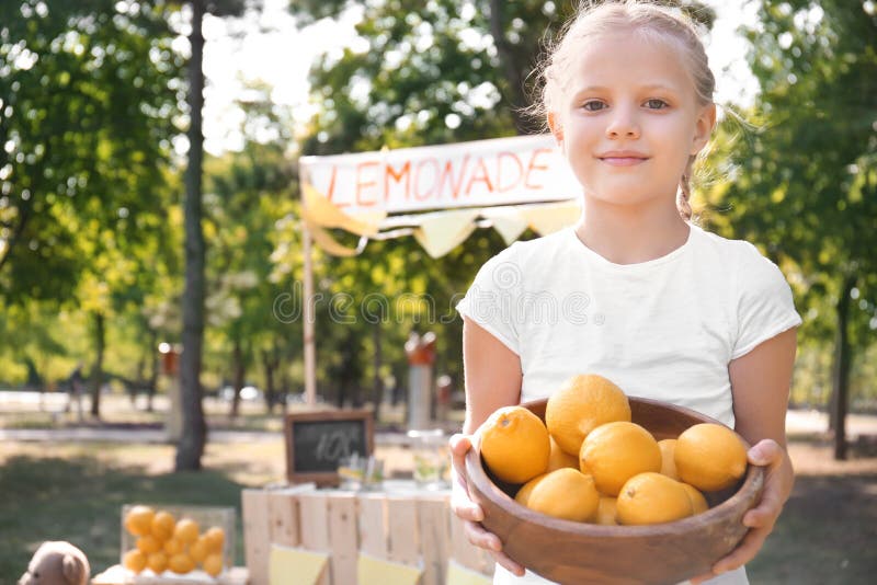 Ciotola della tenuta della bambina con i limoni maturi vicino al supporto in parco immagini stock libere da diritti Ciotola della tenuta della bambina con i limoni maturi vicino al supporto in parco immagini stock libere da diritti