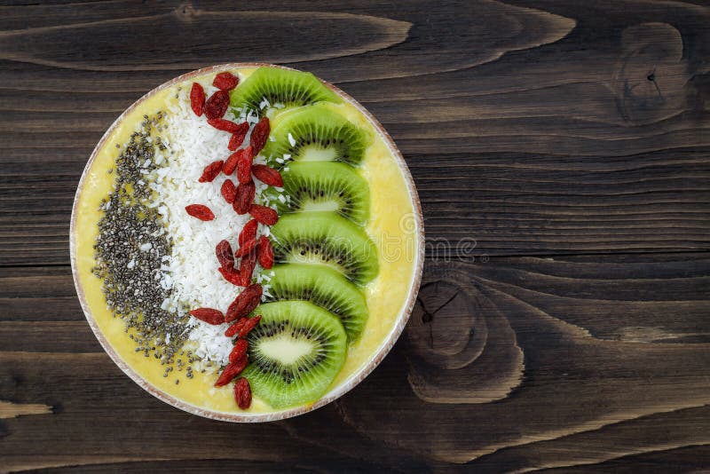 Ciotola gialla del frullato del superfood dell'agrume con il kiwi, semi di chia, noce di cocco, guarnizioni della bacca di goji V fotografia stock libera da diritti Ciotola gialla del frullato del superfood dell'agrume con il kiwi, semi di chia, noce di cocco, guarnizioni della bacca di goji V fotografia stock libera da diritti