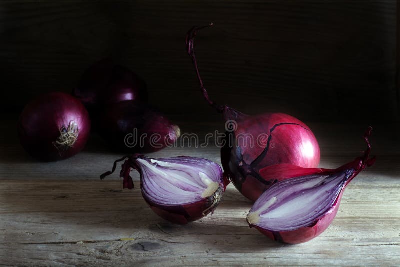 Cipolle rosse intere e divise in due su legno scuro rustico