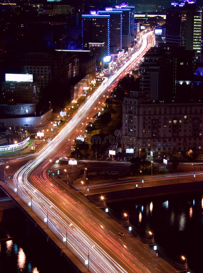 Modern contemporary Russian architecture cityscape: aerial view from above of night megalopolis / city Moscow (Russia) at night / evening with buildings, alight street, streetlight, bridge and river with reflections and traffic - cars look like red and white light trails. Modern contemporary Russian architecture cityscape: aerial view from above of night megalopolis / city Moscow (Russia) at night / evening with buildings, alight street, streetlight, bridge and river with reflections and traffic - cars look like red and white light trails.